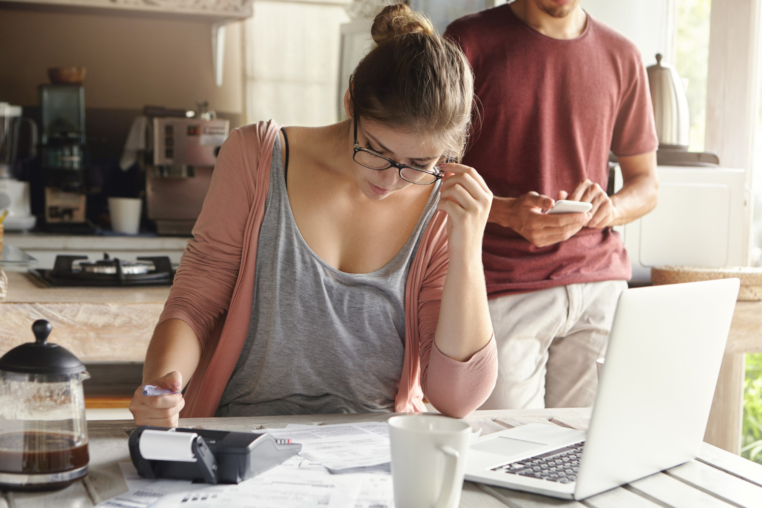Woman calculating down payment funds at kitchen table with partner nearby.