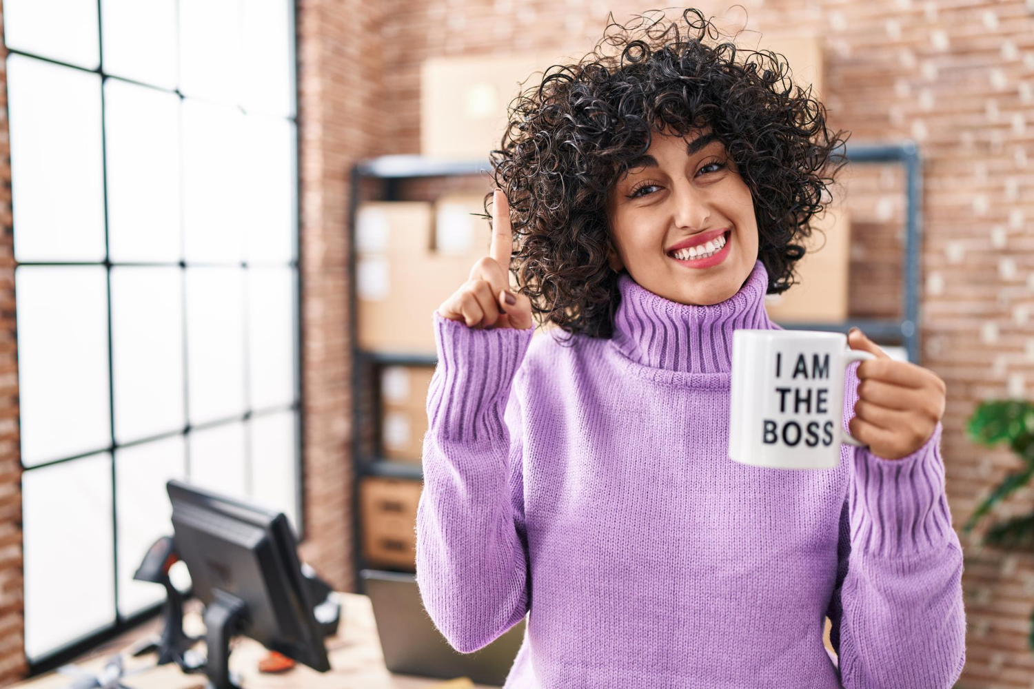 Confident business owner in a modern office holding a mug that says "I am the boss," symbolizing self-employment and leadership.